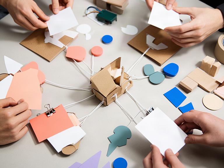 Manos utilizando mapas mentales, tarjetas y piezas cotidianas para construir un prototipo sobre una mesa
